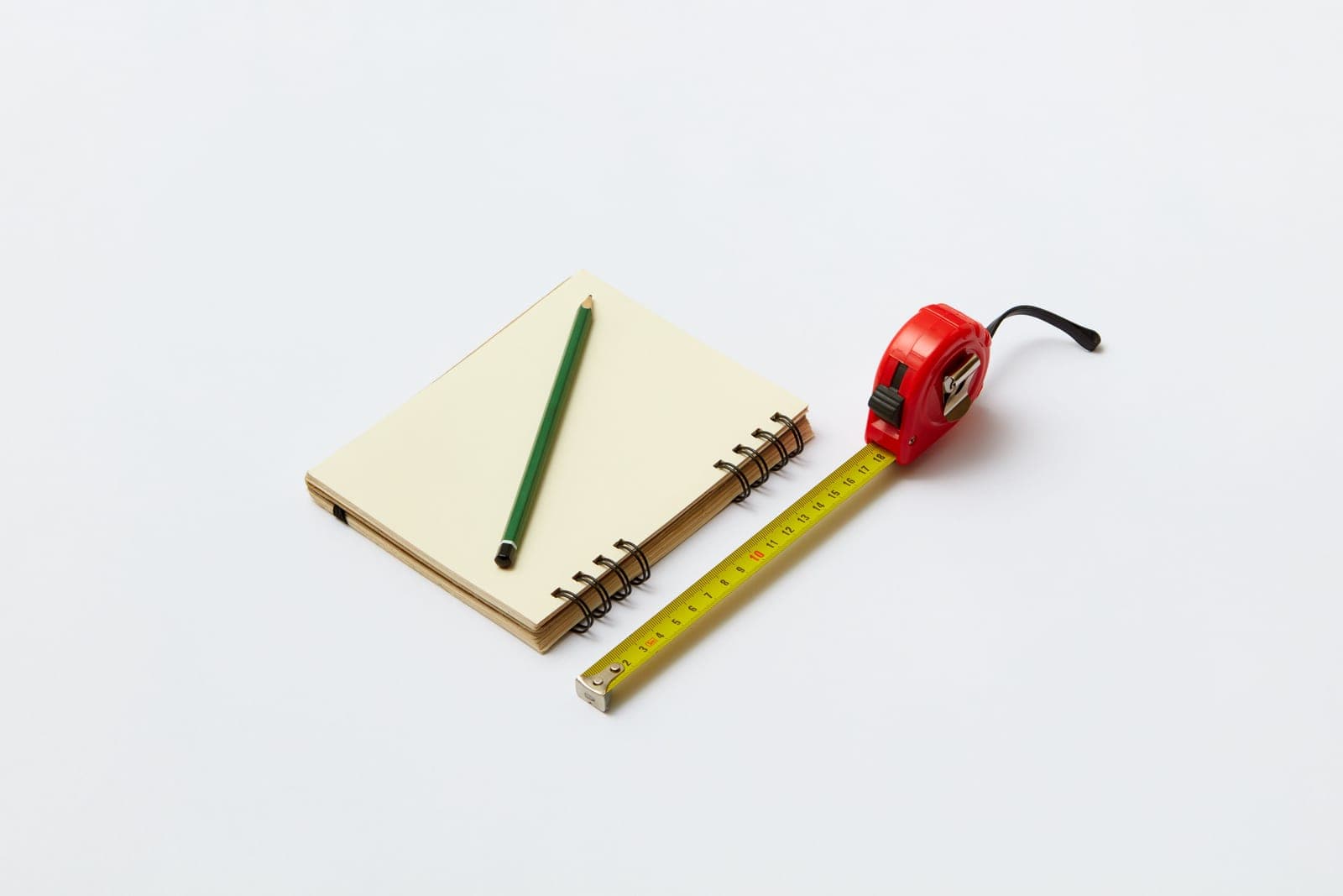 A notebook, pencil and tape measure on a kraft-paper desk surface